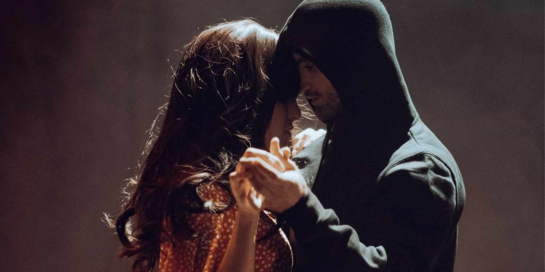 שני אנשים עומדים קרובים מאוד זה לזה, נוגעים יד ביד ובראש, בתוך תאורה רכה ואינטימית המדגישה רגע של קרבה שברירית. האור והצל יוצרים תחושה של ריקוד איטי, מתח רגשי ואהבה שקטה.